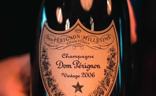 Lähikuva kädestä, jossa on Dom Pérignon Vintage 2006 -samppanjapullo, jossa näkyy koristeltu etiketti, jossa on kultaisia ja mustia yksityiskohtia ja teksti selvästi näkyvissä.