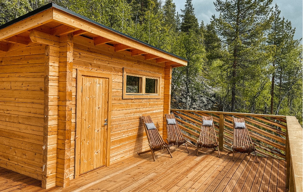 Pieni ikkunaa sisältävä puumökki sijaitsee puiden ympäröimällä terassilla. Terassille on sijoitettu neljä tyynyillä varustettua puista lepotuolia, jotka muodostavat rauhallisen ulkoilma-istumapaikan metsämaisemassa.
