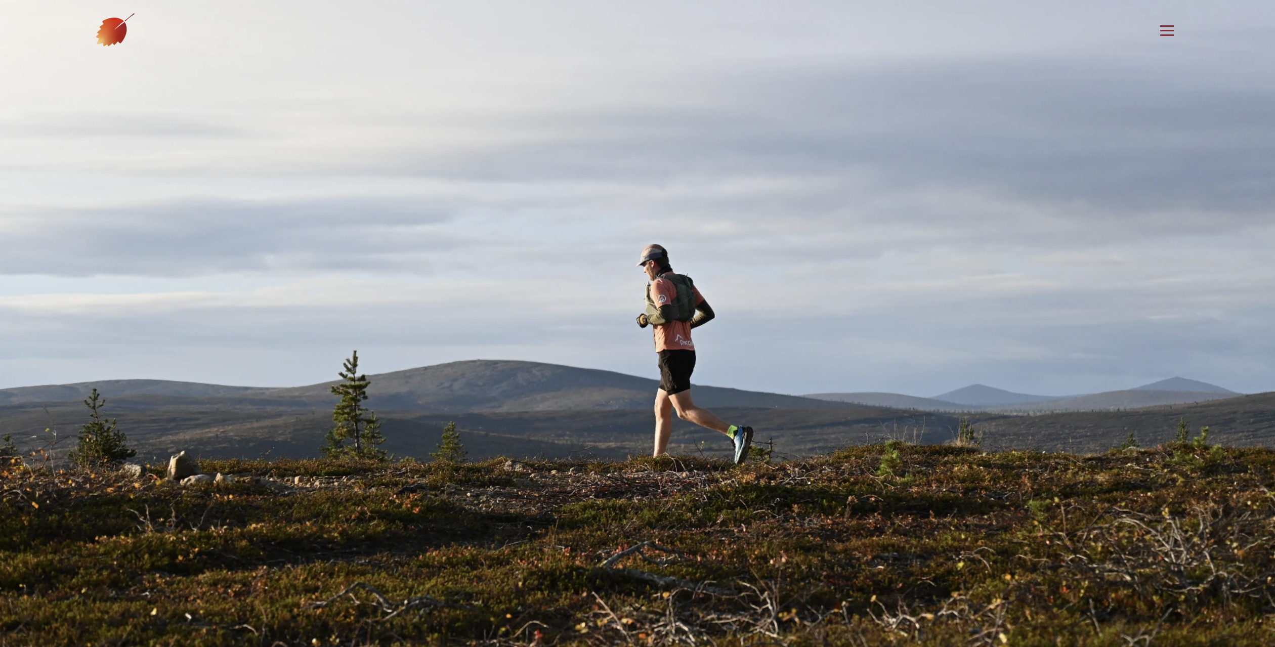 A person in athletic gear runs on a grassy trail with mountains and cloudy skies in the background.