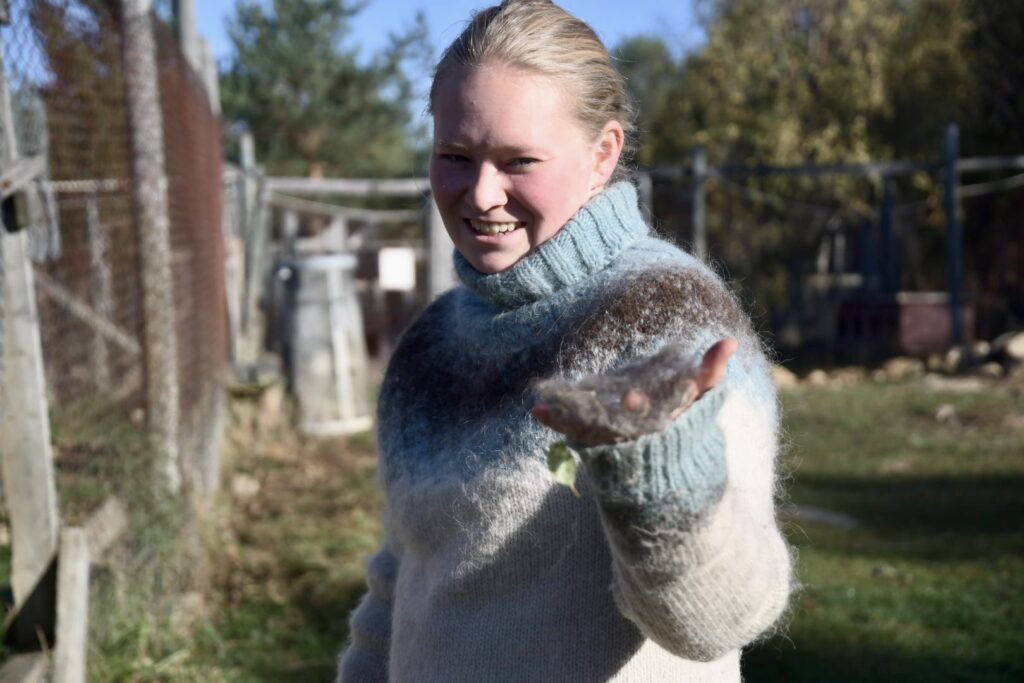 A smiling woman in a blue and white patterned sweater holds a small tuft of animal fur in her hand.