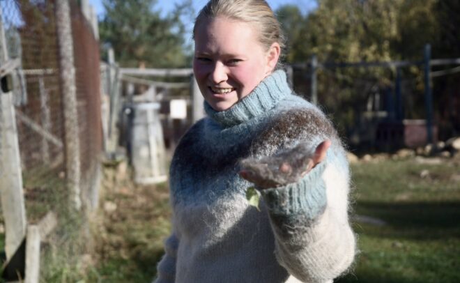 A smiling woman in a blue and white patterned sweater holds a small tuft of animal fur in her hand.