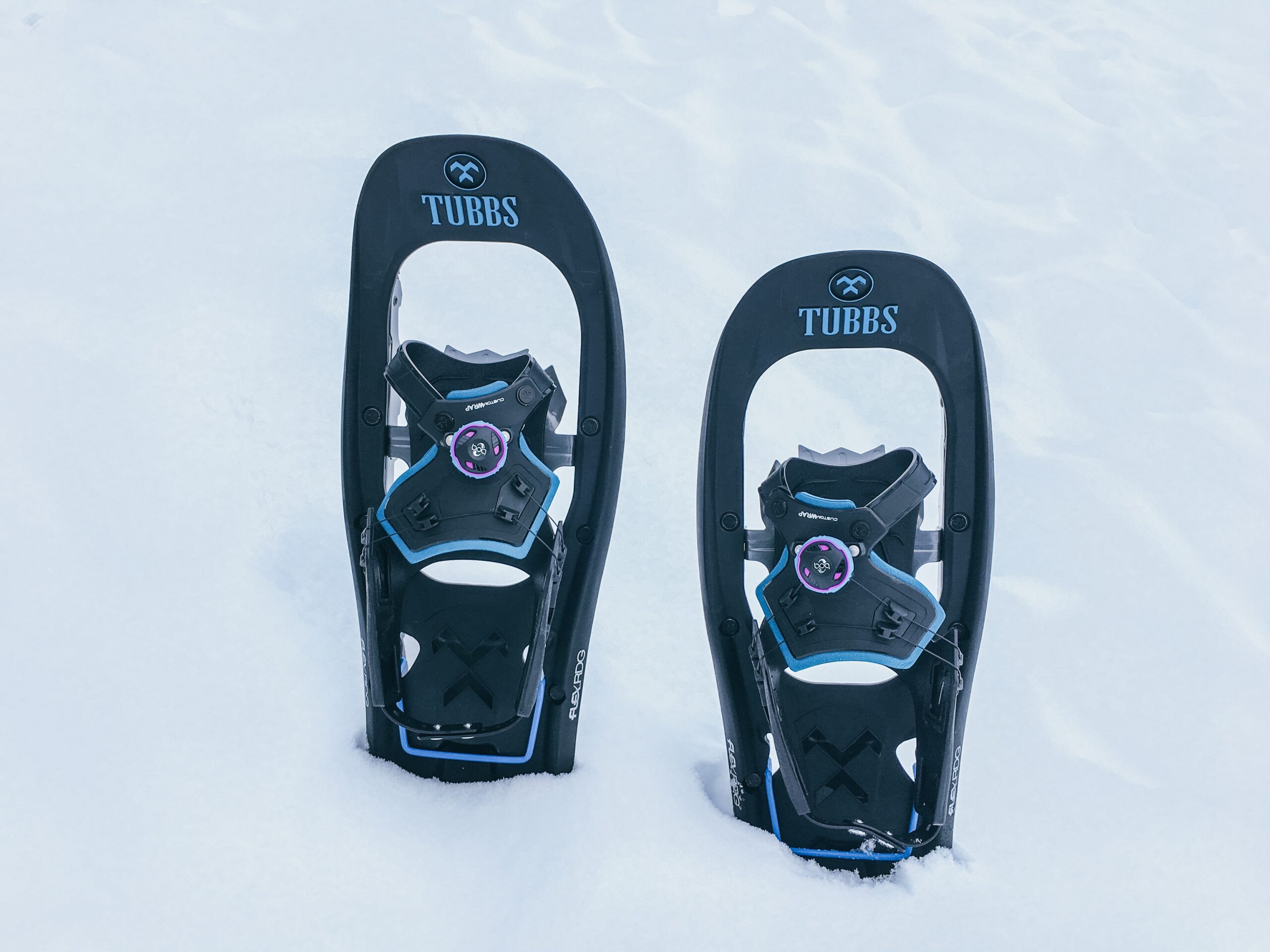 Zwei schwarze Tubbs-Schneeschuhe mit blauen Akzenten, die aufrecht im tiefen Schnee stehen.
